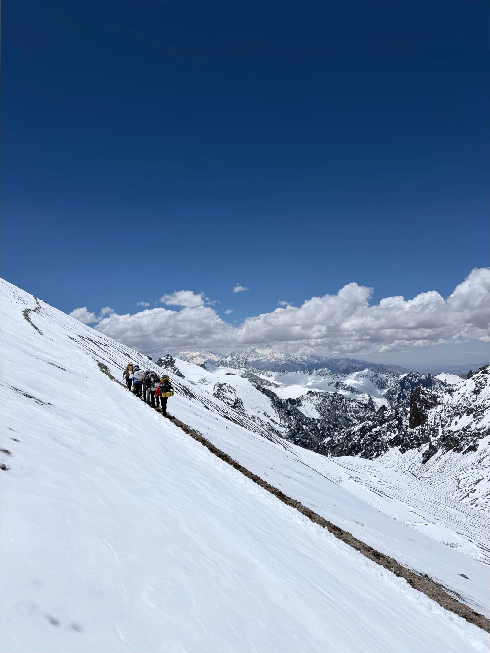 Climbers ascending a steep snow slope with the vast Andes behind