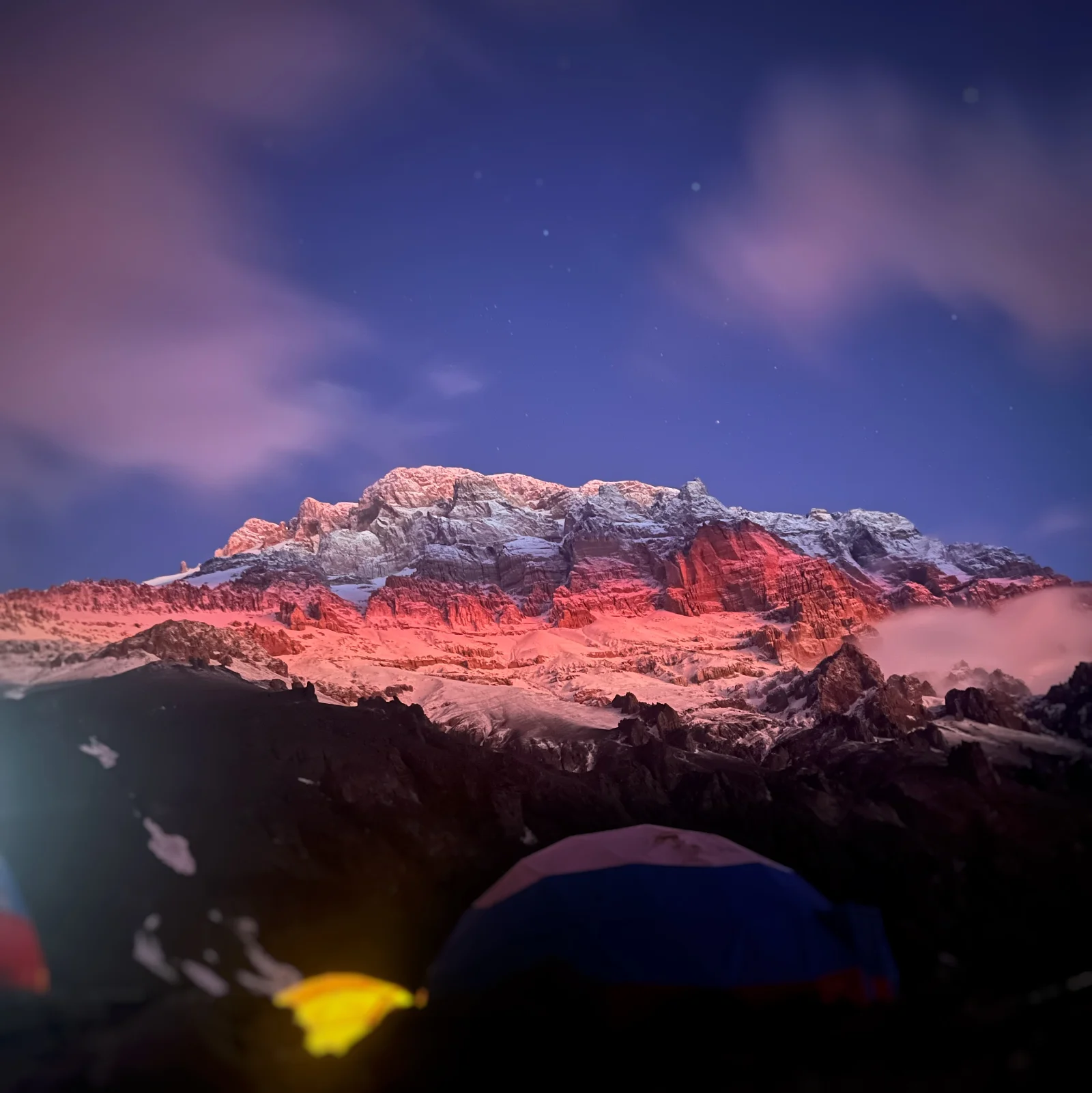 Aconcagua illuminated by alpenglow at night with expedition tents below
